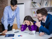 Zwei Männer und eine Frau diskutieren mit Blick auf Unterlagen. Die Frau stützt den Kopf in die Hände.